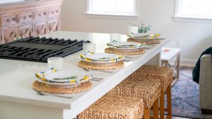 A kitchen island with a built-in stove, a white countertop, and a series of woven stools.
