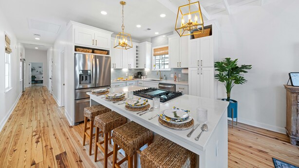A modern kitchen with white cabinetry, a central island with stools, stainless steel appliances, and decorative lighting.
