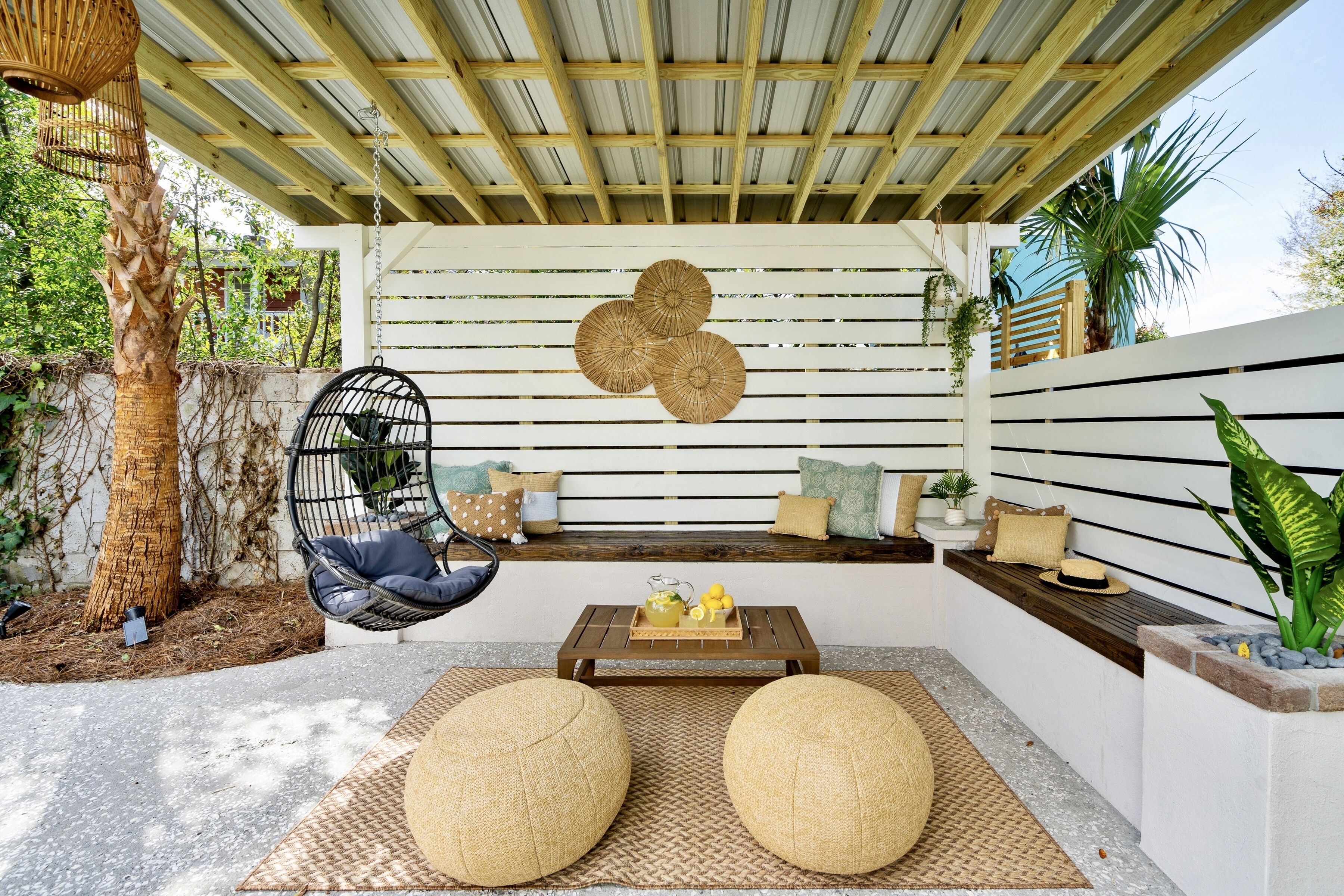 A cozy outdoor seating area with a wooden bench, woven poufs, and a hanging chair.