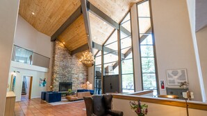 A spacious living area with a stone fireplace, large windows, and a high ceiling.