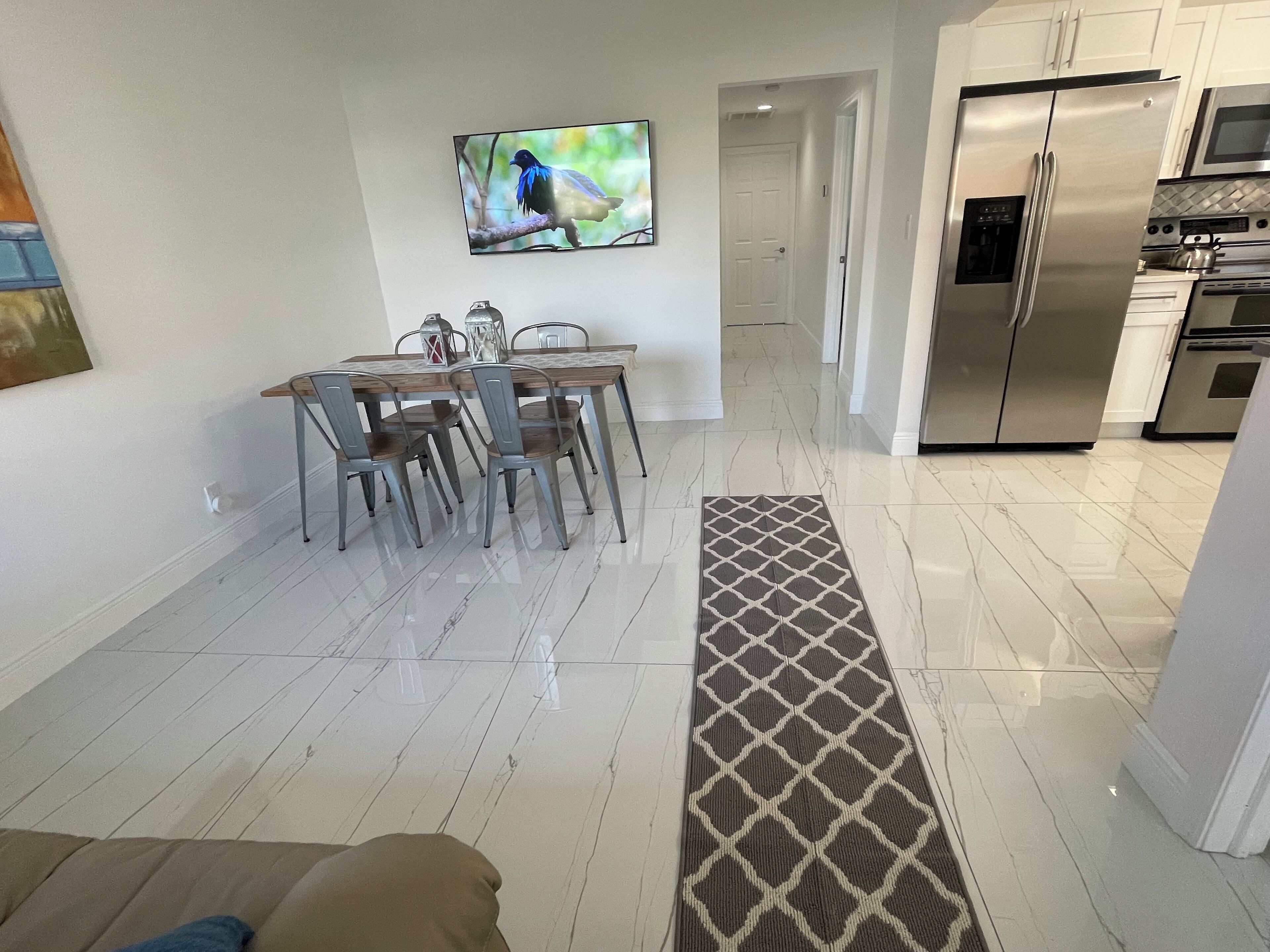 Een moderne keuken met roestvrijstalen apparatuur, een eethoek met een houten tafel en metalen stoelen, en een aan de muur bevestigde televisie.