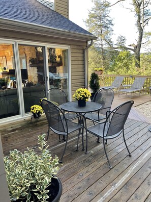 A wooden deck with a round table and chairs, surrounded by potted plants and a view of the house interior. - Cliff’s End • Ski & Golf Views • Fire Pit • Game Room (Basye)