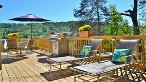 Una terraza de madera con mobiliario exterior, incluyendo sillas, una mesa y una parrilla.