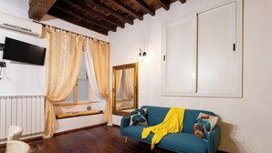 A living room with a blue sofa, a white radiator, a TV, and a window with curtains. - Signoria - Flo Apartments (Firenze)