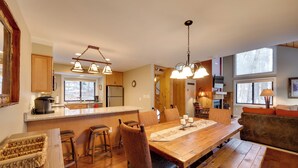 A spacious kitchen with wooden countertops, a large island, and pendant lighting. There is a dining area with a wooden table and chairs, and a cozy seating area with a sofa and cushions. - Lincoln Condo w/ Balcony & View < 2 Mi to Loon Mtn (Lincoln)