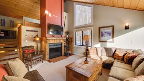 A cozy living room with a fireplace, wooden furniture, and large windows. - Lincoln Condo w/ Balcony & View < 2 Mi to Loon Mtn (Lincoln)