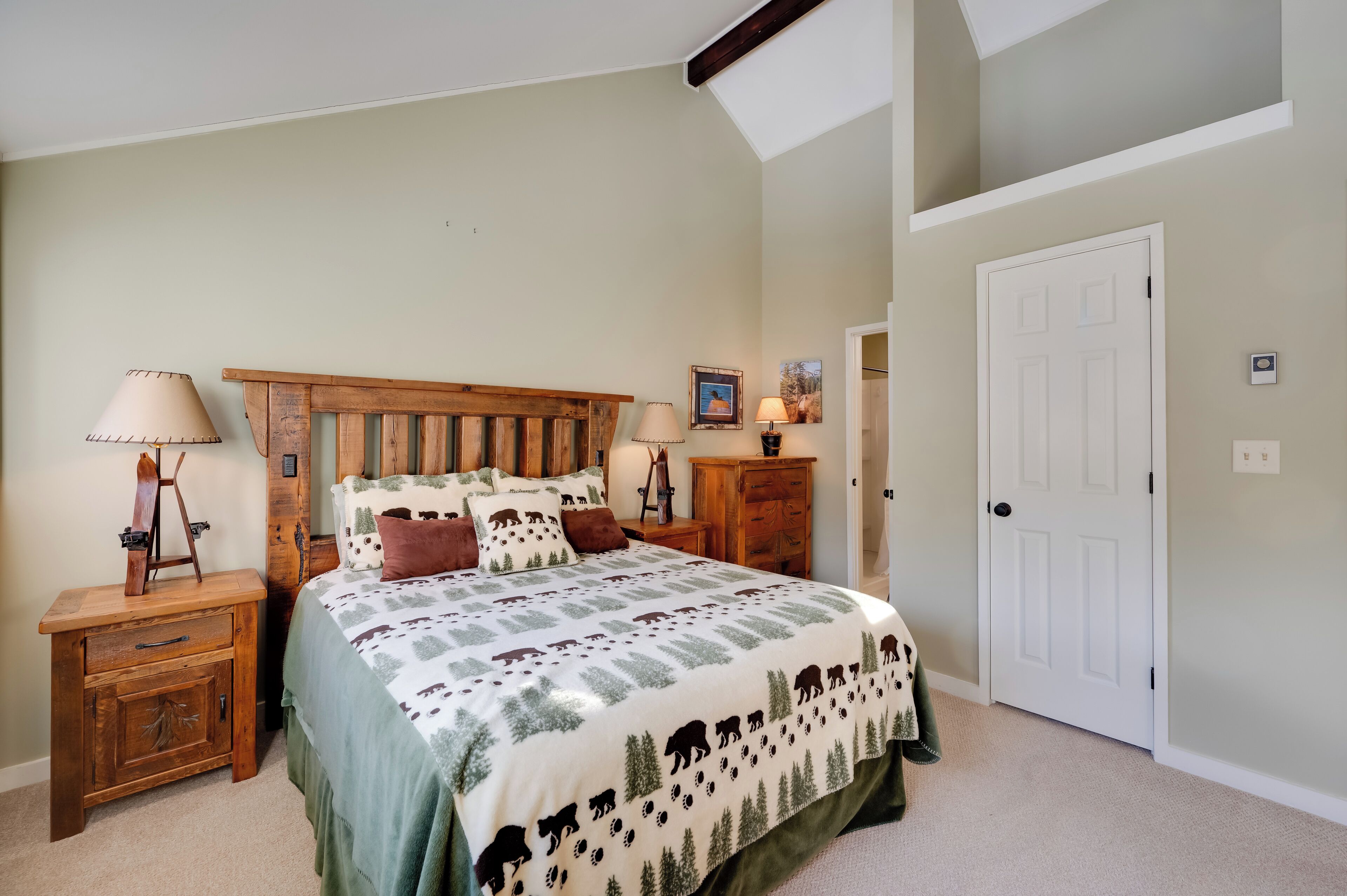 A bedroom with a large bed, wooden headboard, two bedside tables with lamps, a nightstand, and a door.