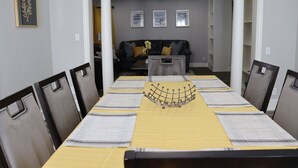A dining room with a long table set for six, flanked by chairs, with a yellow table runner and a decorative metal piece in the center. - Chisholm Creek by Top Golf 2 (Oklahoma City)