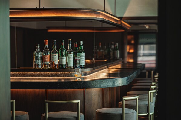 A bar area with a curved counter, multiple bottles of liquor, and bar stools. - Marufukuro (Kyoto)