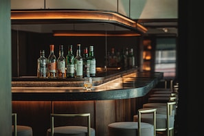 Una zona de bar con una barra curva, varias botellas de licores y taburetes.