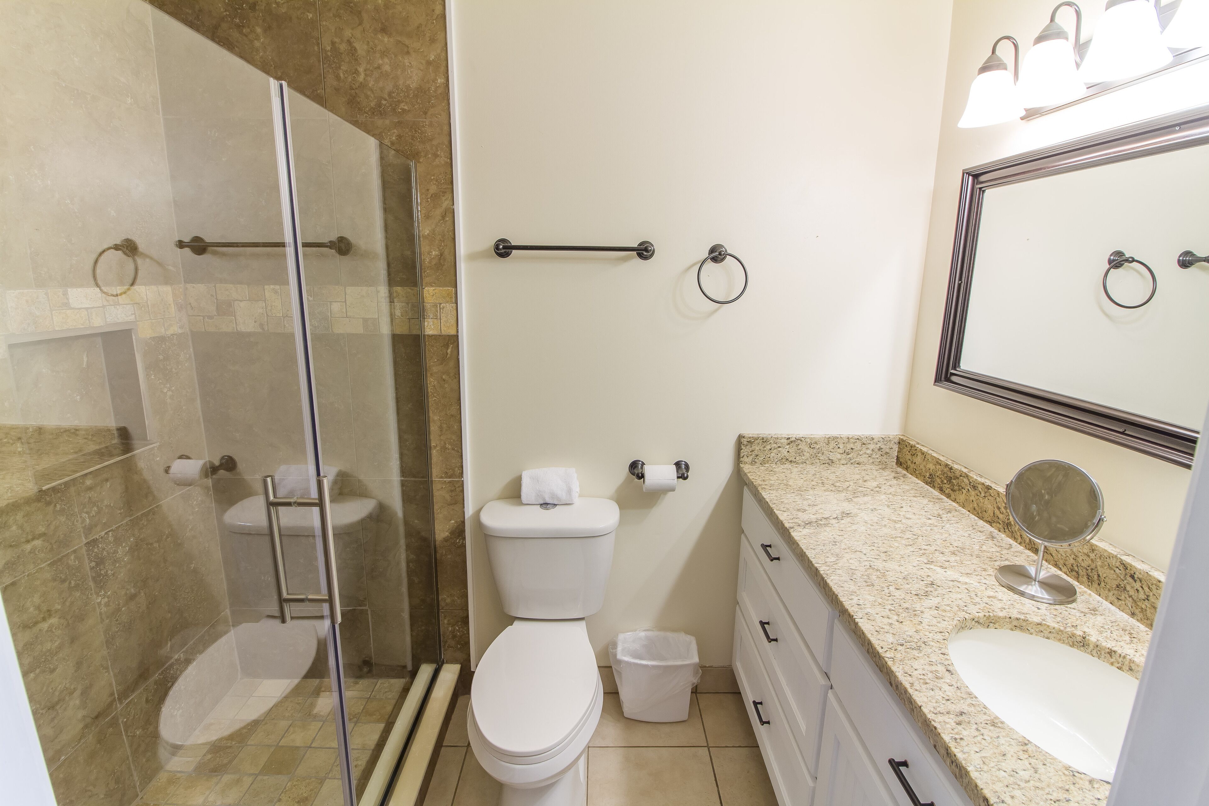 A bathroom with a glass shower enclosure, a toilet, a sink with a mirror, and a vanity with drawers.