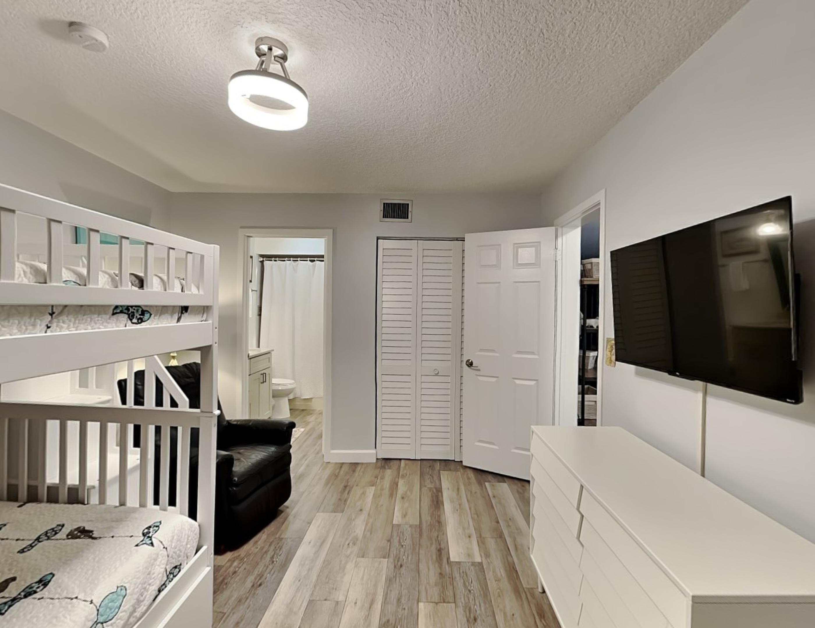 A room with bunk beds, a TV, a closet, and a door leading to a bathroom.