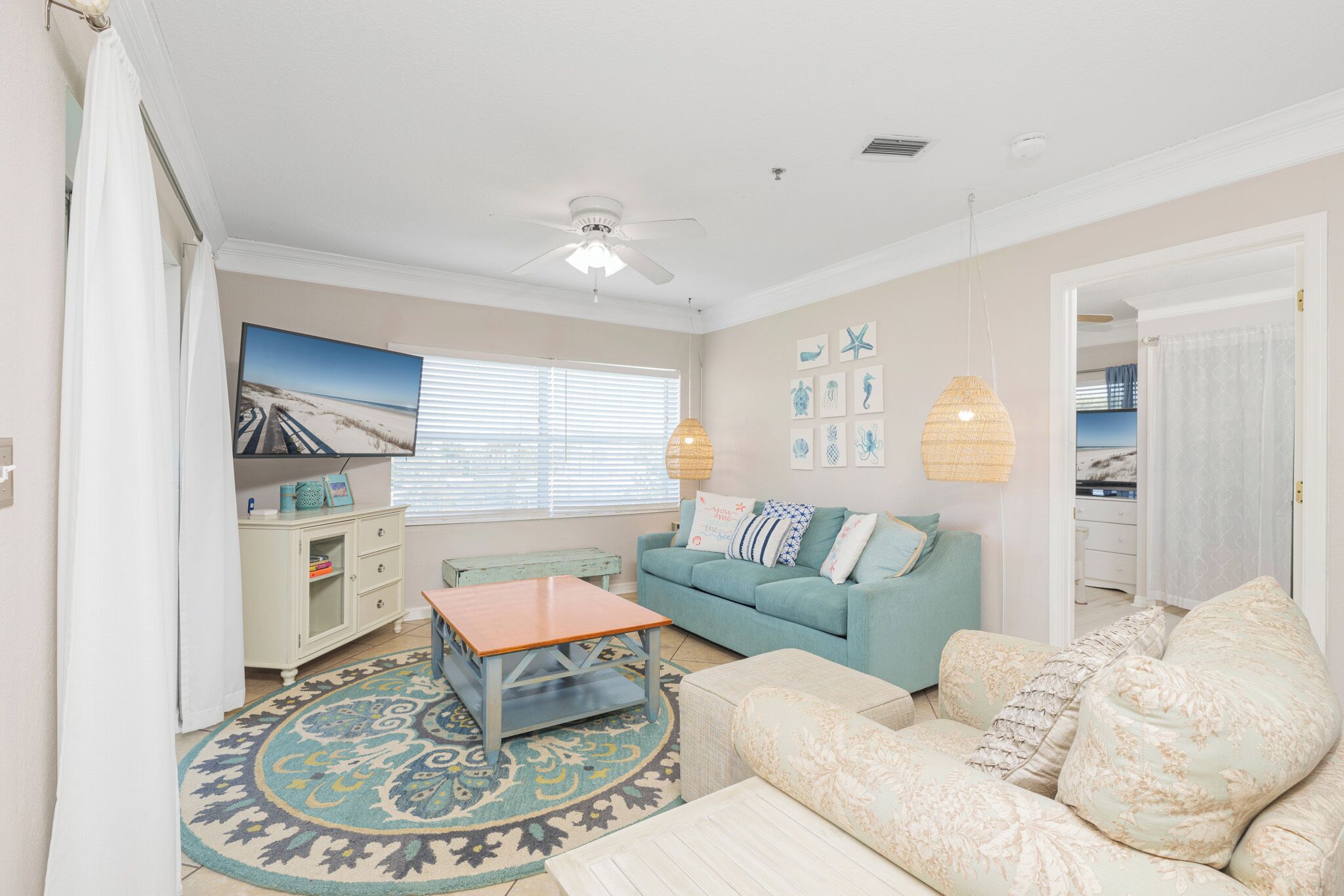 A living room with a teal sofa, a wooden coffee table, a patterned rug, and a ceiling fan.