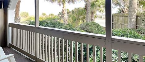 A covered porch with a white railing, a white chair, and a view of palm trees and greenery.