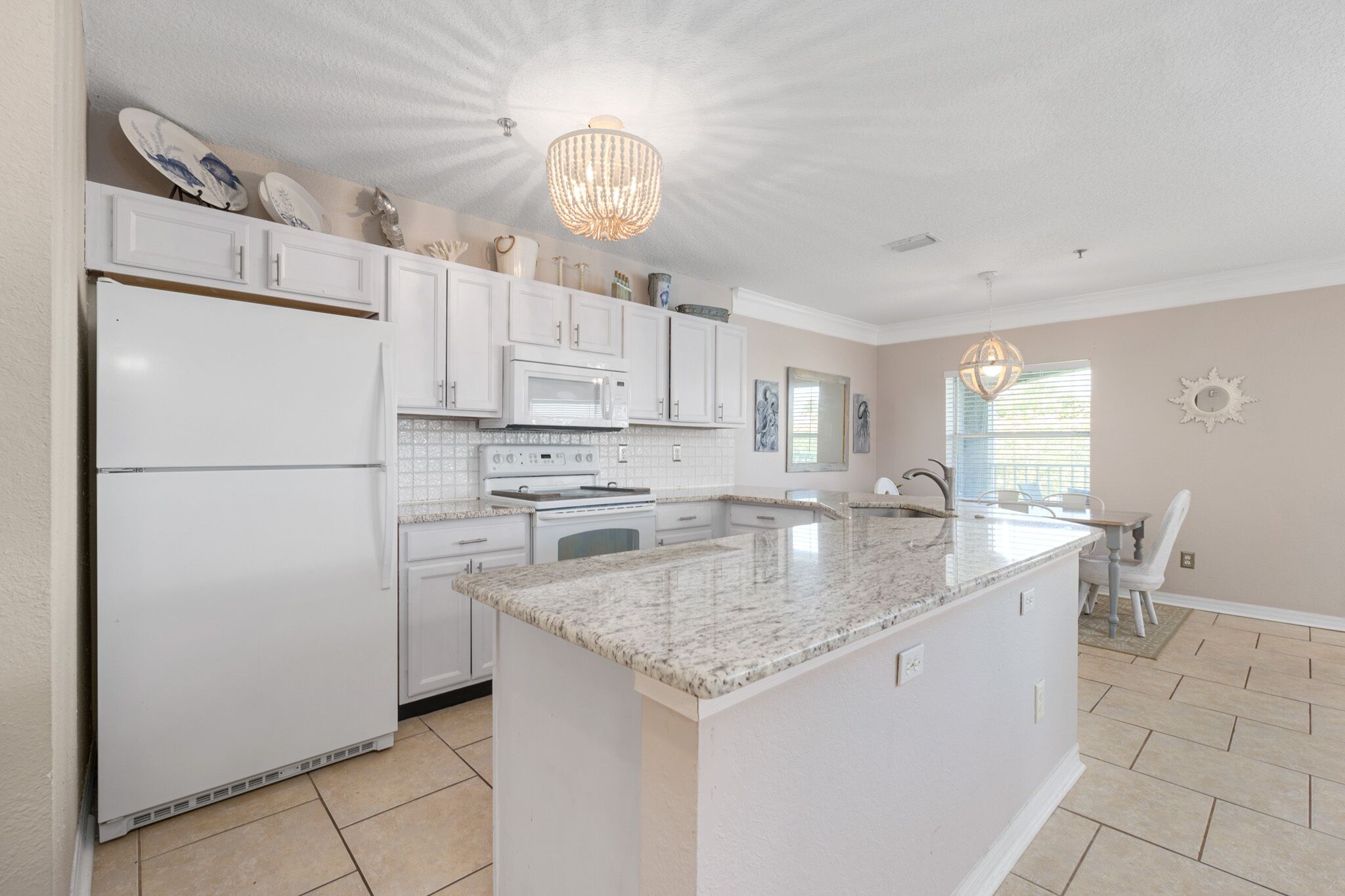 A modern kitchen with white cabinetry, a granite countertop island, and a chandelier.
