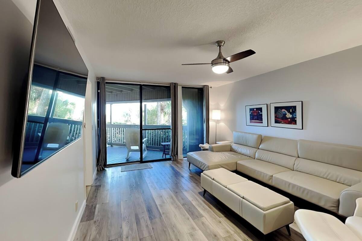 A modern living room with a sectional sofa, a ceiling fan, and a sliding glass door leading to a balcony.