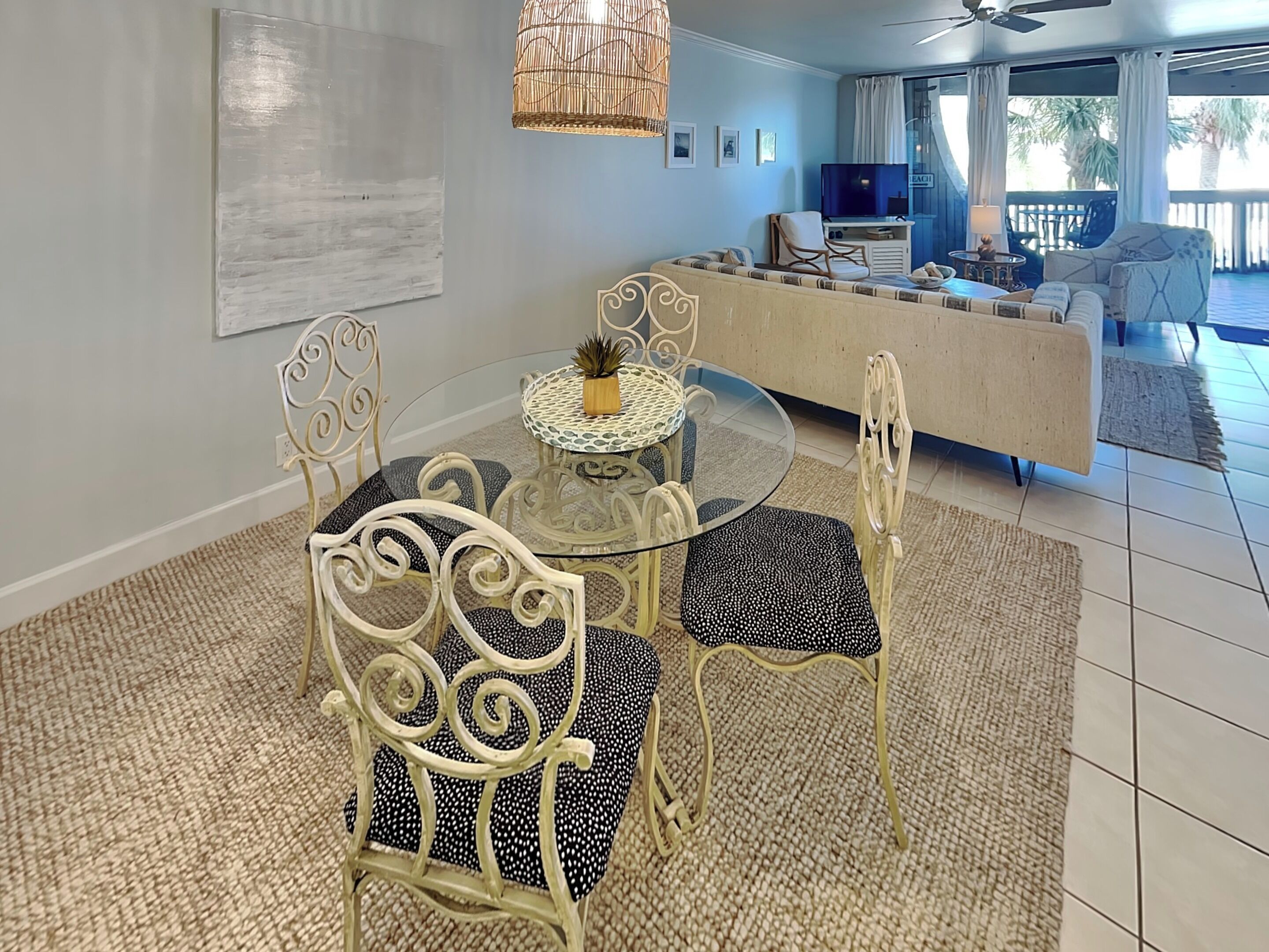 A dining area with a glass table and metal chairs, a sofa, a TV, and a view of the outdoors.