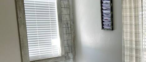 A bedroom with a window, a bed with patterned bedding, a wall-mounted light, and a curtain.