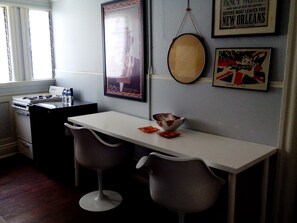 A kitchen with a white countertop, two grey bar stools, a stove, and a framed poster on the wall. - Historic Alvarado Terrace (Los Angeles)
