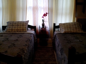 A room with two beds, each with patterned bedding and matching pillows. There is a small table with a vase of flowers between the beds. - Historic Alvarado Terrace (Los Angeles)