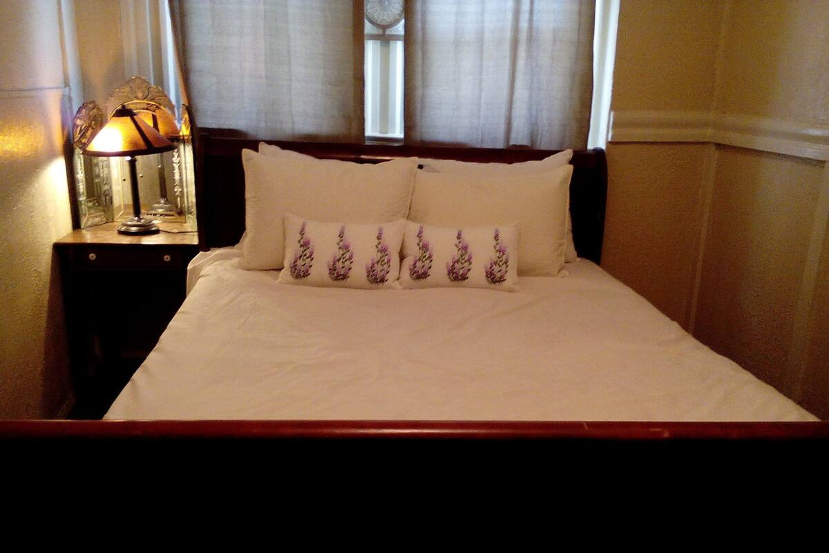 A neatly made bed with floral pillows, a bedside lamp, and a window with curtains.