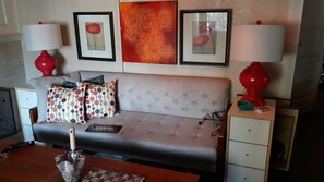 A living room with a grey sofa, patterned cushions, a coffee table, and two red lamps. There are framed artworks on the wall and a small cabinet with drawers. - Historic Alvarado Terrace (Los Angeles)