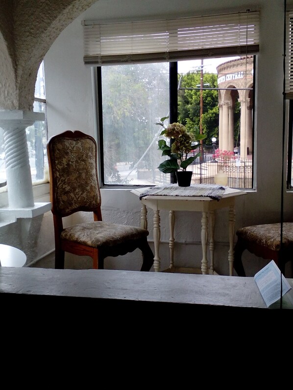 A room with a large window, a chair, a small table, and a potted plant. - Historic Alvarado Terrace (Los Angeles)