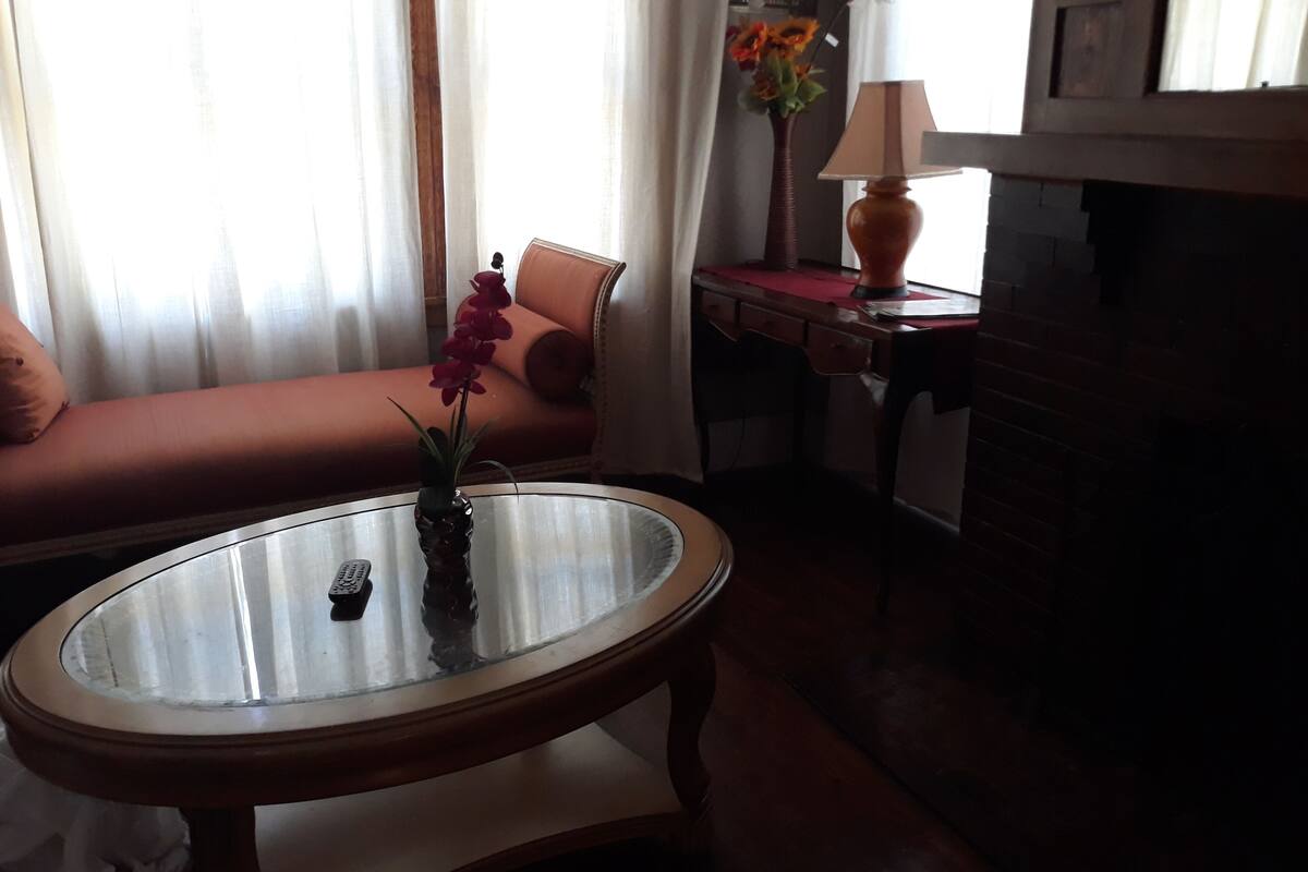 A living room with a sofa, a glass coffee table, a lamp, and a vase with flowers.