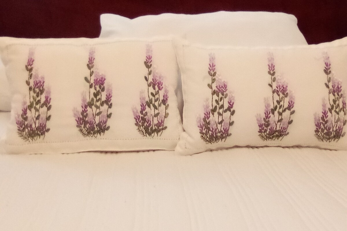A bed with white bedding and pillows featuring embroidered floral designs.