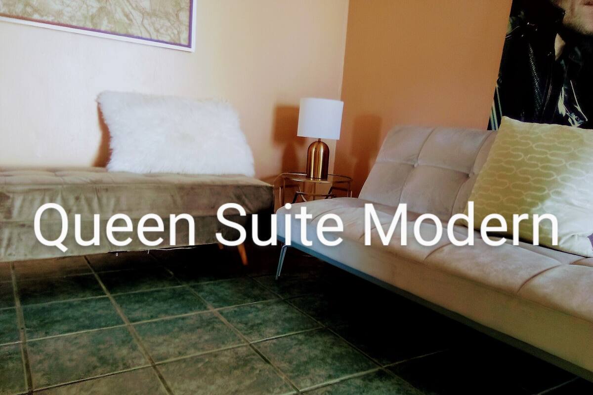 A modern queen suite with a bed, a sofa, and a nightstand with a lamp.