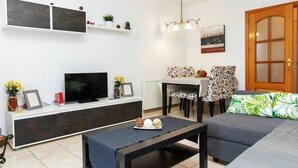 Ein modernes Wohnzimmer mit Flachbildfernseher, Essecke mit Tisch und Stühlen, Sofa und Holztür.