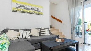 Ein modernes Wohnzimmer mit einem grauen Ecksofa, einem schwarzen Couchtisch und einer Treppe, die zu einem Außenbereich führt.