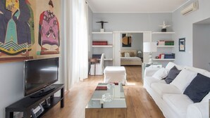 Ein modernes Wohnzimmer mit Flachbildfernseher, einem weißen Sofa, einem Glastisch und einem Bücherregal.