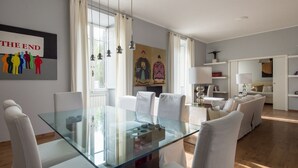 Ein modernes Wohnzimmer mit einem Glastisch, weißen Stühlen, einer Couch und einem Gemälde an der Wand.