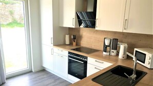 Une cuisine moderne avec des armoires blanches, un plan de travail en bois, un four encastré, un four à micro-ondes, une machine à café et un évier.