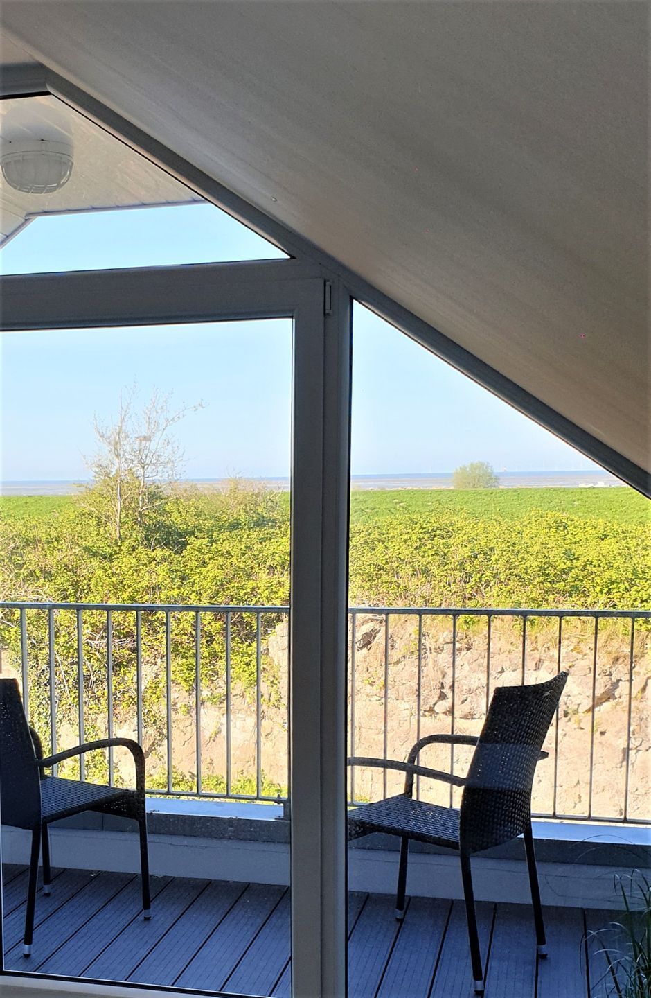 A balcony with two chairs, a view of a green field, and a clear sky.