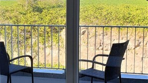 Un balcon avec deux chaises, une vue sur un champ verdoyant et un ciel dégagé.