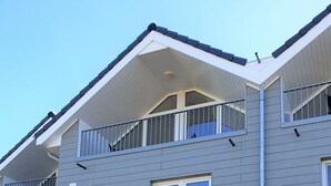 Un immeuble résidentiel moderne à deux étages, avec une façade grise, des éléments décoratifs blancs et un balcon à l’étage supérieur.