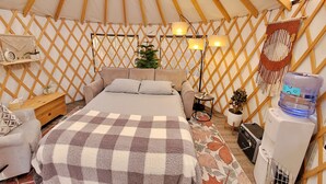 A cozy, well-lit tent with a bed, bedside table, lamp, and a water dispenser. - Hideaway Glamping Yurt  (Bellingham)