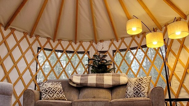A yurt interior with a central circular skylight, a sofa with patterned cushions, and three wall-mounted lamps. - Hideaway Glamping Yurt  (Bellingham)