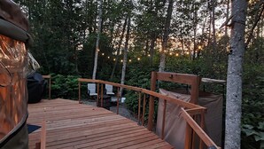 A wooden deck with a railing, surrounded by trees and string lights. - Hideaway Glamping Yurt  (Bellingham)