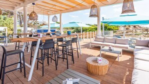 An outdoor dining area with wooden tables and chairs, hanging wicker lamps, and a round wooden stool. - Cosy apartment in villa for 4 people with A/C, WIFI, pool and terrace (Porto Cesareo)