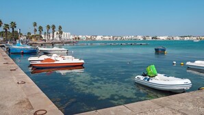 A marina with various boats docked, a clear blue sky, and a coastal town in the background. - Cosy apartment in villa for 4 people with A/C, WIFI, pool and terrace (Porto Cesareo)