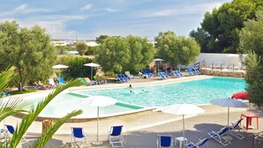 A pool area with multiple lounge chairs and umbrellas, surrounded by trees and a clear sky. - Cosy apartment in villa for 4 people with A/C, WIFI, pool and terrace (Porto Cesareo)