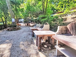 Un espace extérieur aménagé avec des bancs et des tables en pierre, entouré d’arbres et de verdure.