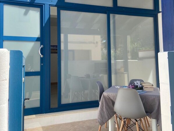 A room with a sliding glass door leading to an outdoor area, a table with chairs, and a small table with books and flowers.