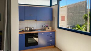 Eine kleine Küche mit blauen Schränken, einem Gasherd und einem Fenster mit Blick auf eine Wohngegend.