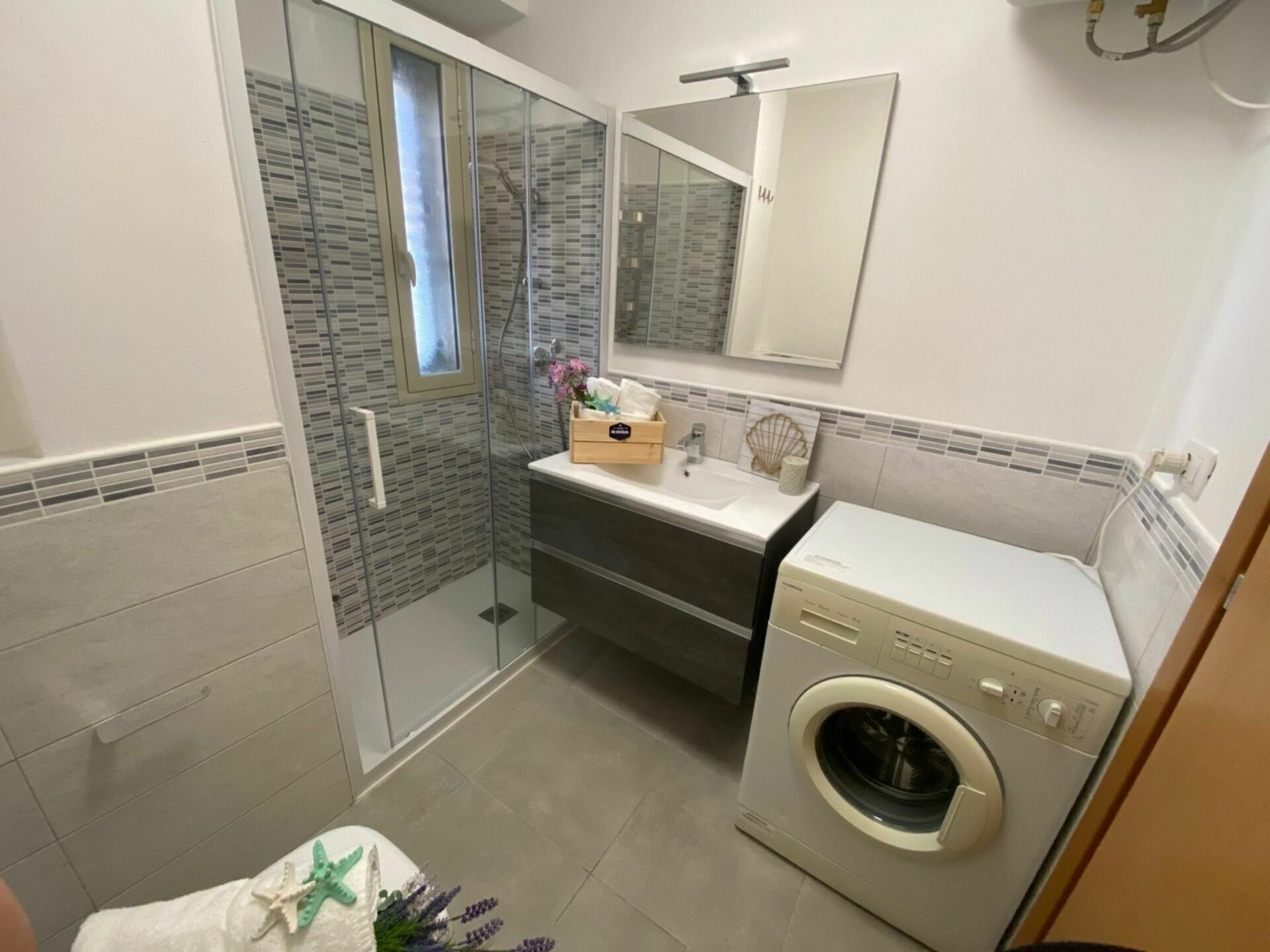 A modern bathroom with a glass-enclosed shower, a sink with a mirror, and a built-in washing machine.