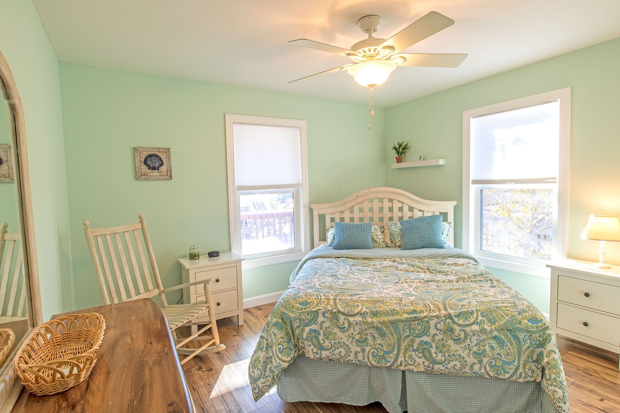 A bedroom with a bed, a ceiling fan, a window, a chair, a nightstand, and a lamp.