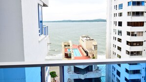 Udsigt fra en balkon over et swimmingpool og havet, med høje bygninger i baggrunden.